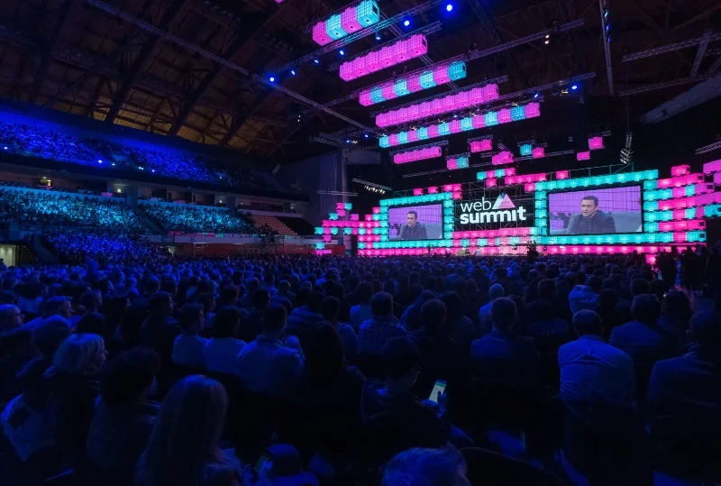 "Web Summit Qatar 2025 event showcasing a large audience and an illuminated main stage with speakers."