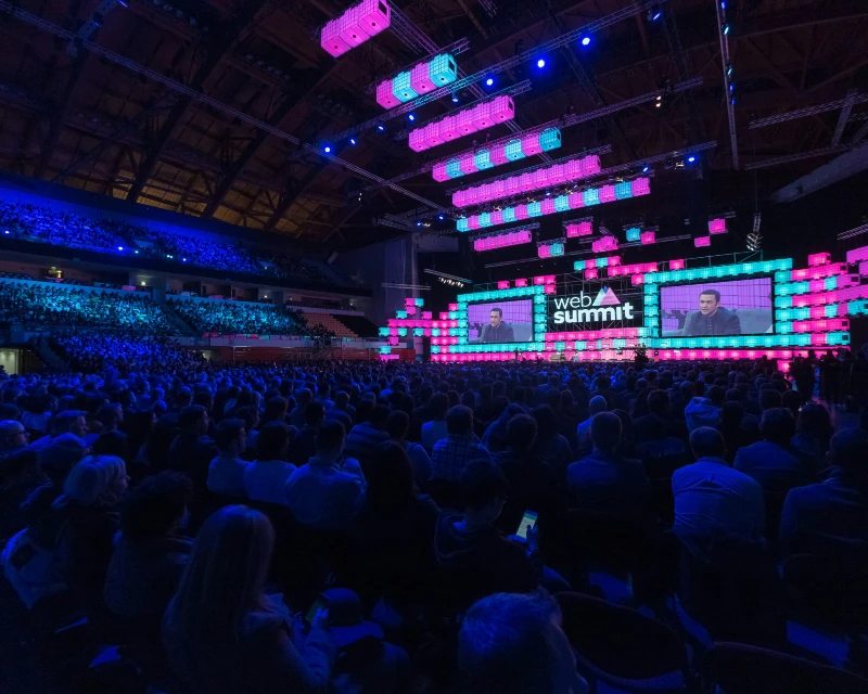 "Web Summit Qatar 2025 event showcasing a large audience and an illuminated main stage with speakers."