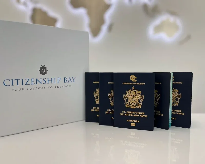 A row of St. Kitts and Nevis passports placed beside a Citizenship Bay box, promoting the Caribbean citizenship by investment program.
