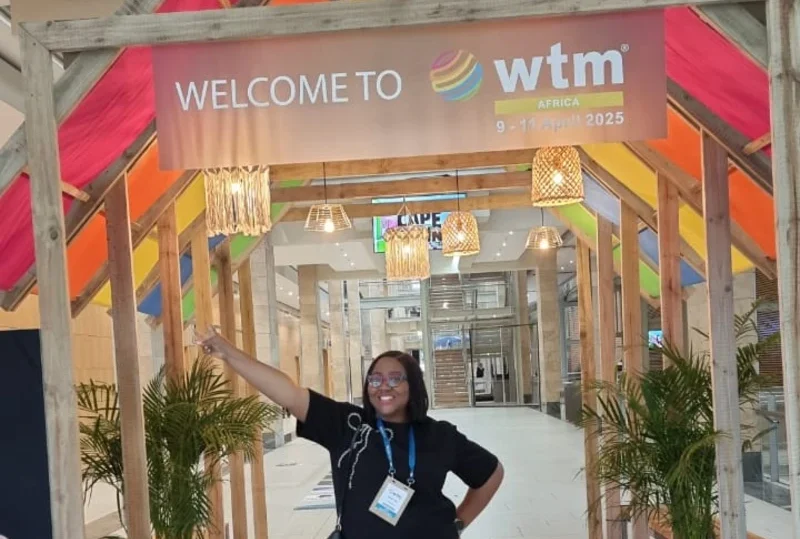 A smiling woman representing Lery Hago poses under the “Welcome to WTM Africa 2025” banner at the Cape Town International Convention Centre.