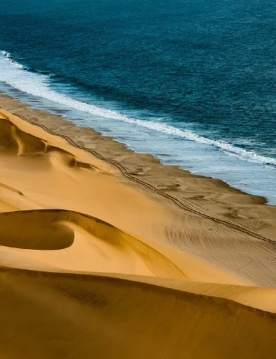 A breathtaking view of golden sand dunes meeting the Atlantic Ocean in Namibia, showcasing the country’s natural beauty and investment potential.