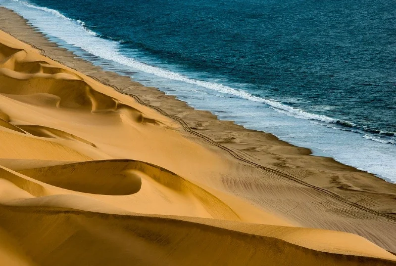 A breathtaking view of golden sand dunes meeting the Atlantic Ocean in Namibia, showcasing the country’s natural beauty and investment potential.