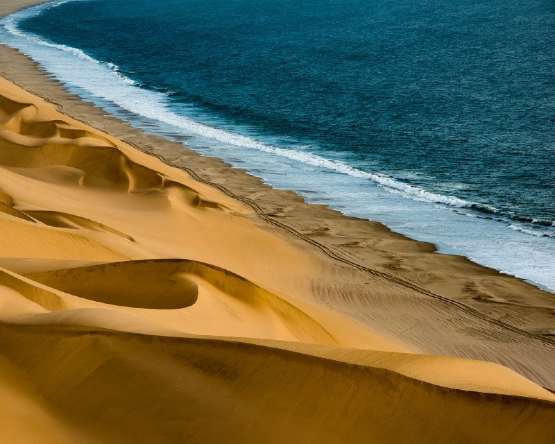A breathtaking view of golden sand dunes meeting the Atlantic Ocean in Namibia, showcasing the country’s natural beauty and investment potential.
