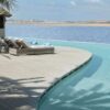 "Infinity pool merging with the sea horizon, featuring sun loungers on a wooden deck by a straw hut, embodying a Marrakech Love Getaway destination from www.leryhago.com."