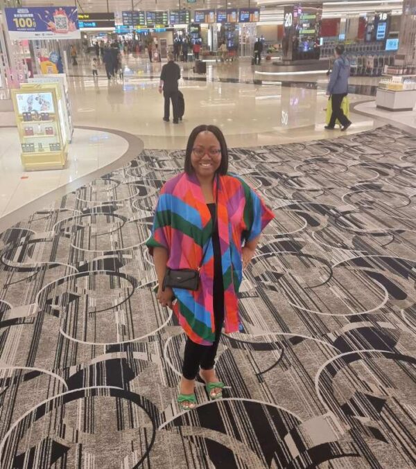 "A smiling woman in a colorful kaftan standing in the chic interior of Singapore Changi Airport, ready to begin her luxury getaway."