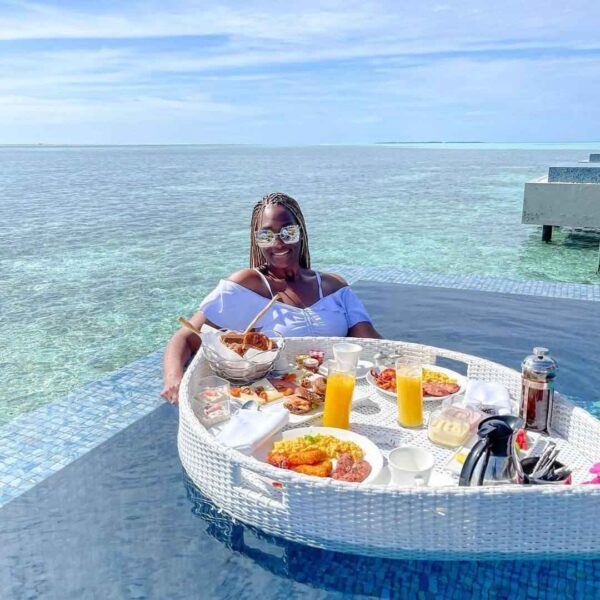 "Woman enjoying a lavish brunch on a floating table at a romantic villa in the Maldives, with a serene ocean backdrop, perfect for couples seeking a tranquil getaway. Visit www.leryhago.com to book your Maldives Romantic Villa Stay."