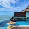 "A couple shares a tender moment during a luxurious floating brunch in an infinity pool overlooking the Maldivian sea. Experience romantic villa stays with www.leryhago.com."