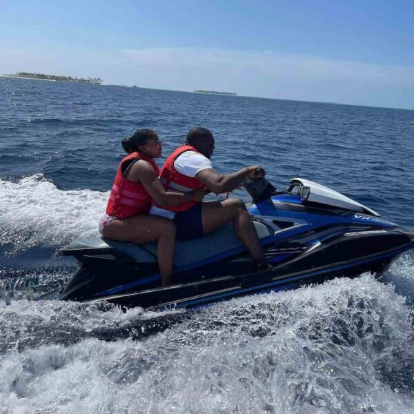 "A couple in life jackets enjoys a thrilling jet ski ride on the blue waters of the Maldives, capturing the adventurous side of a romantic villa stay. Book your adventure at www.leryhago.com."