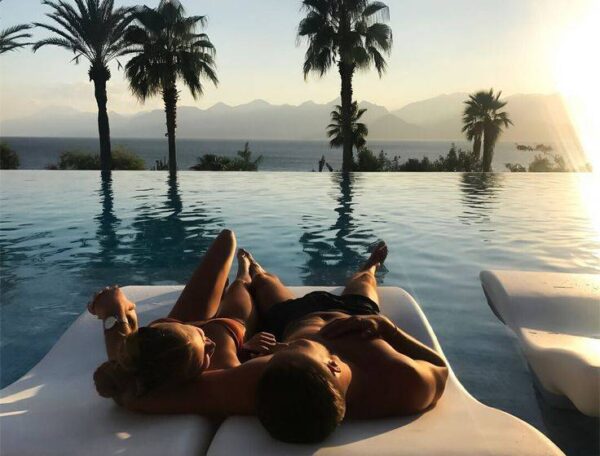"A couple relaxing on a float at an infinity pool overlooking a mountain range during sunset, epitomizing the Paris Love Getaway experience."