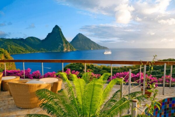 "Luxurious Christmas St. Lucia Package - Breathtaking balcony view of the Pitons during sunset, with vibrant flowers and elegant seating arrangement, available at www.leryhago.com"