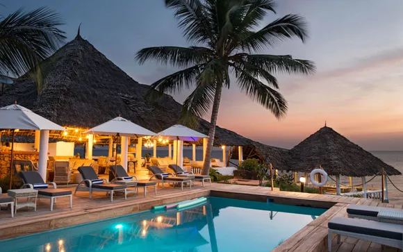 "Luxurious poolside view at dusk with thatched-roof huts and palm trees, part of a Zanzibar Festive Season Getaway package."
