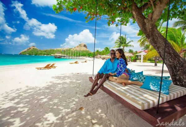 "A couple enjoying the Luxurious Christmas St. Lucia Package, relaxing on a swing set against a pristine beach backdrop, available at www.leryhago.com"