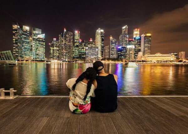 "A couple sits close together, enjoying the stunning view of Singapore's skyline at night, illuminated with festive lights for Christmas."