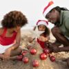 "Family in Christmas hats building a sandcastle decorated with red ornaments on Mombasa beach"