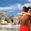 "Happy couple hugging on a tropical beach with unique rock formations in the background."