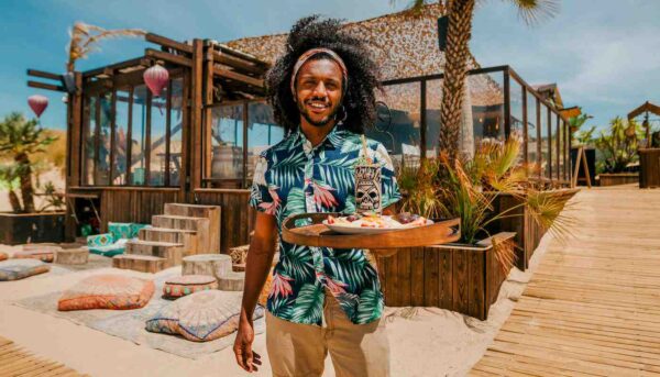 "A smiling host with a tropical shirt serving a platter of refreshments at a Lisbon Cultural Getaway beach lounge - leryhago.com"