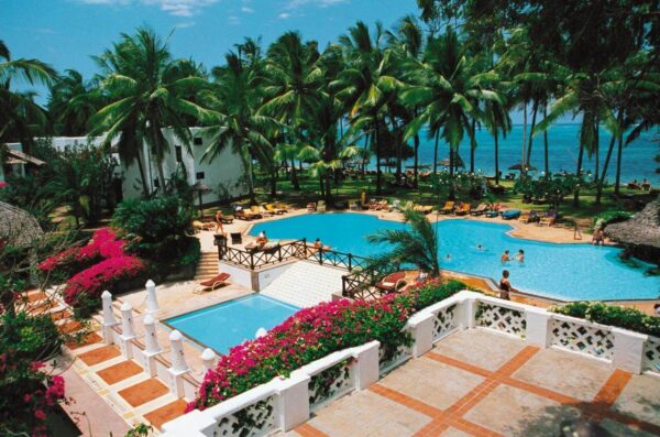 "Tranquil luxury resort pool surrounded by lush palms and traditional thatched huts in Mombasa"