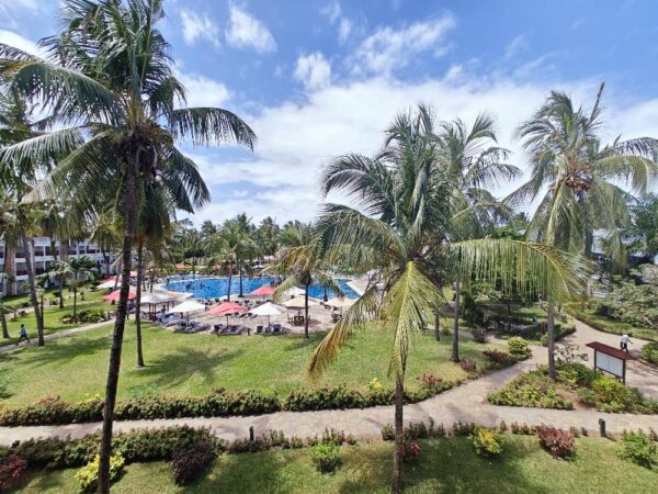 "An idyllic view of a poolside retreat with lush palm trees and manicured gardens, under the sunny skies of Nairobi Mauritius, inviting a Pre-Christmas Escape."