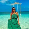 "A woman in a flowing green dress stands on the pristine shores of the Maldives, with the 'SANDELI' sign swinging above the turquoise sea, embodying the peaceful solitude of a romantic villa stay. Discover more at www.leryhago.com."