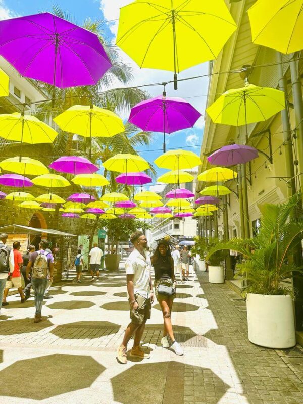 A couple walks hand in hand under a canopy of vibrant yellow and pink umbrellas, celebrating Pre-Christmas Magic in Mauritius."
