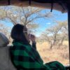 "A woman in a chic green plaid wraps reflects on the serene savannah from a safari jeep in Nairobi Mauritius, embodying the tranquil essence of a Pre-Christmas Escape."