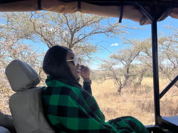 "A woman in a chic green plaid wraps reflects on the serene savannah from a safari jeep in Nairobi Mauritius, embodying the tranquil essence of a Pre-Christmas Escape."