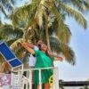 "A couple in harmonizing green attire strikes a Titanic-like pose on a white lookout deck, surrounded by lush palm trees at a Nigerian Romantic Resort."