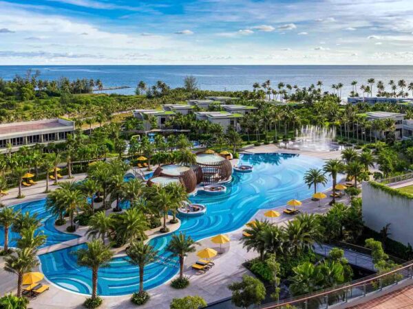 "Aerial view of a luxurious resort in Vietnam featuring a sprawling pool, palm trees, and oceanfront, perfect for a romantic getaway package."