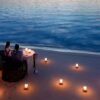 "A couple enjoys a romantic candlelit dinner on the beach, with candles in the sand and the ocean's gentle waves in the twilight."