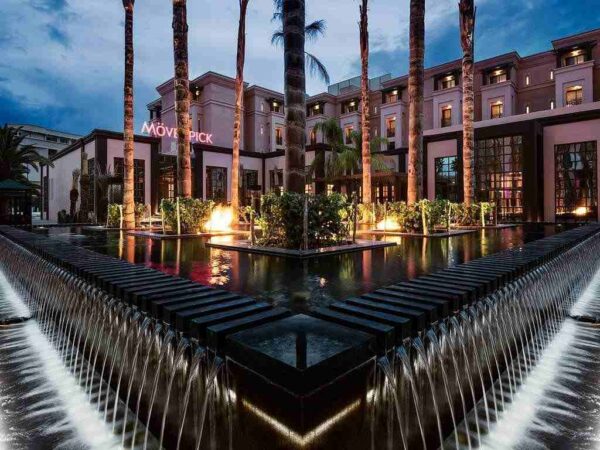 "Mövenpick hotel exterior at dusk with illuminated fountains and palm trees, offering a sophisticated venue for a Marrakech Love Getaway, featured by www.leryhago.com."