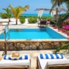 "Luxury poolside loungers with a straw hat, tropical flowers, and a view of the turquoise sea in a bright, sunny resort setting."