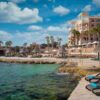 "Upscale beach resort in Malta with loungers and thatched umbrellas by the clear Mediterranean Sea, part of the Malta Historical Getaway, visit www.leryhago.com."