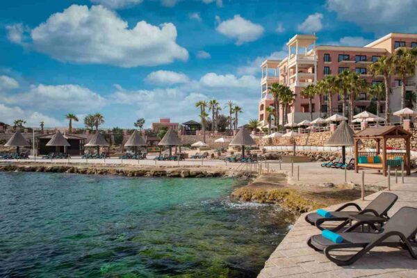 "Upscale beach resort in Malta with loungers and thatched umbrellas by the clear Mediterranean Sea, part of the Malta Historical Getaway, visit www.leryhago.com."