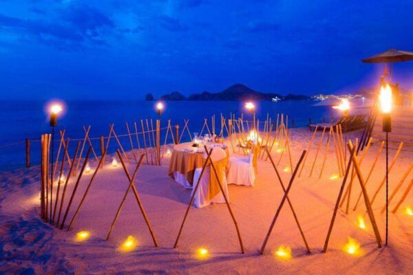 "A romantic beach dinner setup with torches and candles, perfect for an intimate Venice Valentine's Getaway evening - reserve at www.leryhago.com."