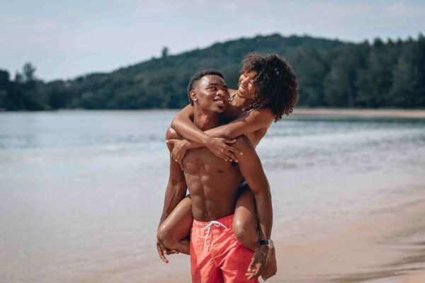 "Joyful Black couple embracing on a tranquil beach, capturing the bliss of a Paris Love Getaway, moments curated by www.leryhago.com."