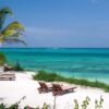 "Beach loungers under a palm tree overlooking the serene turquoise waters of Zanzibar, an ideal festive season retreat."