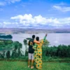 "A couple in vibrant attire overlooks the tranquil waters of Lake Kivu, with the lush hills of Rwanda in the distance, capturing the serene Rwanda Radiance - explore more at www.leryhago.com."
