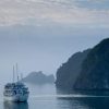 A luxury cruise ship sailing through the misty waters of Halong Bay with limestone karsts in the background.