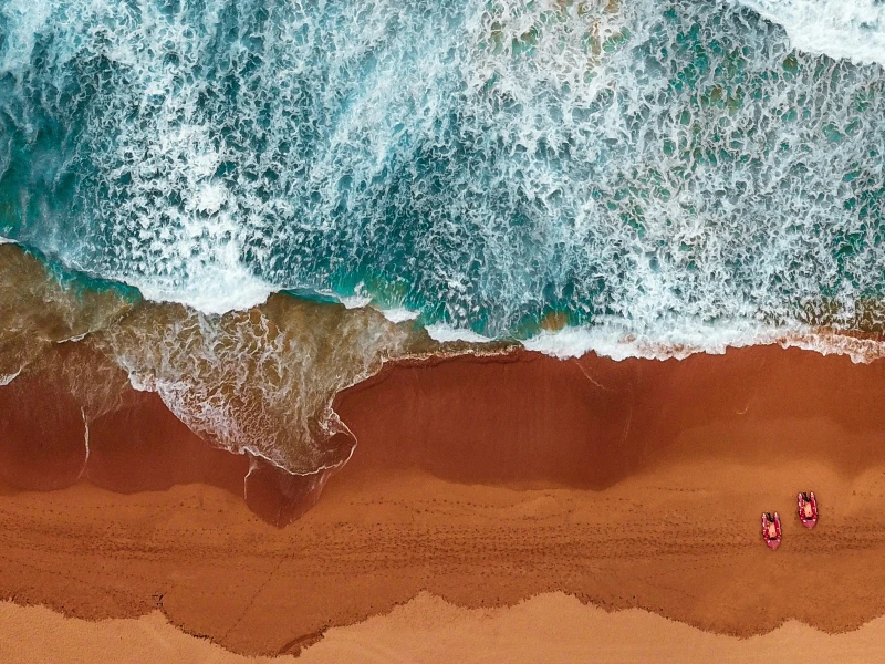 Aerial view of waves crashing onto a sandy beach with two beach chairs, ideal for a relaxing honeymoon getaway in 2025.