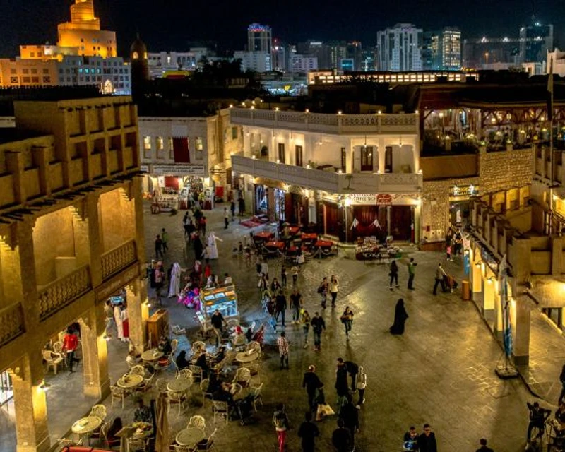 An evening view of Souq Waqif in Qatar, with people shopping, dining, and exploring the lively marketplace under the city lights.