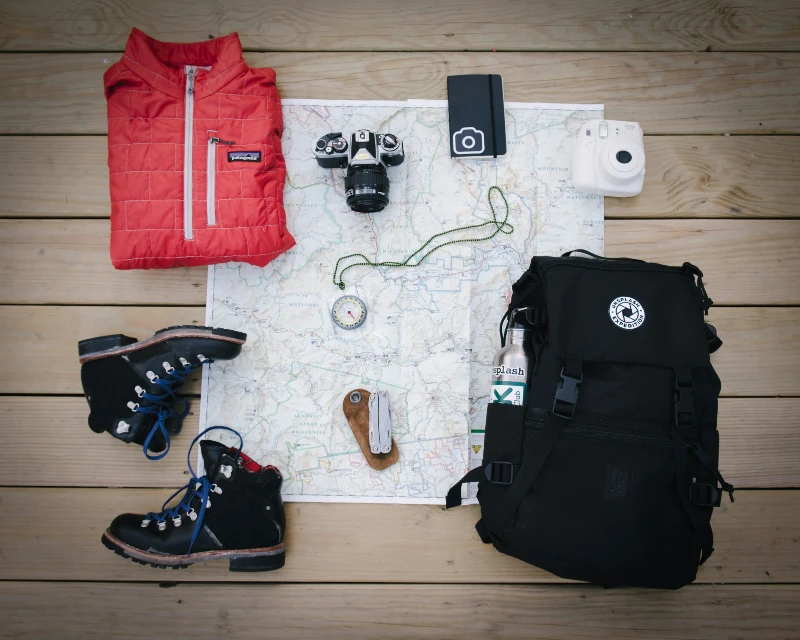 Solo travel essentials including a red jacket, hiking boots, cameras, compass, and backpack for a stress-free journey with Lery Hago Travels.