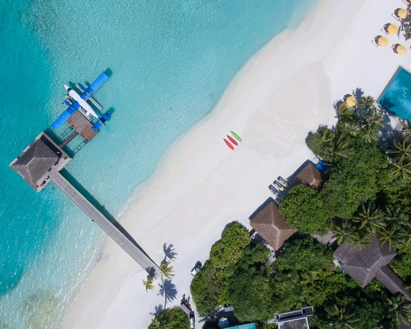 "A stunning aerial view of a Maldives luxury beach resort with crystal-clear waters, kayaks, and a seaplane docked at the pier, ideal for first-timers with Lery Hago Travels."