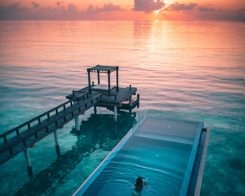 "A serene sunset in the Maldives with a luxury infinity pool overlooking the ocean, perfect for first-time visitors seeking a luxury escape with Lery Hago Travels."