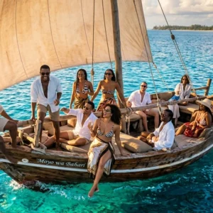 An elevated, cinematic drone shot captures a traditional wooden dhow boat sailing through the crystal-clear, vibrant turquoise waters of Zanzibar. Onboard, a group of stylish African men and women in their late 20s and 30s celebrate under a warm golden hour sun. They are dressed in elegant resort wear, including white linen shirts, patterned sarongs, and summer hats. One man sits prominently at the bow, joyfully waving toward the camera, while others lounge on the deck, laughing and enjoying the breeze. The large, weathered sail is filled with wind, and the surrounding ocean transitions from a glowing electric teal to a deep sapphire, creating a luxurious and aspirational travel aesthetic.