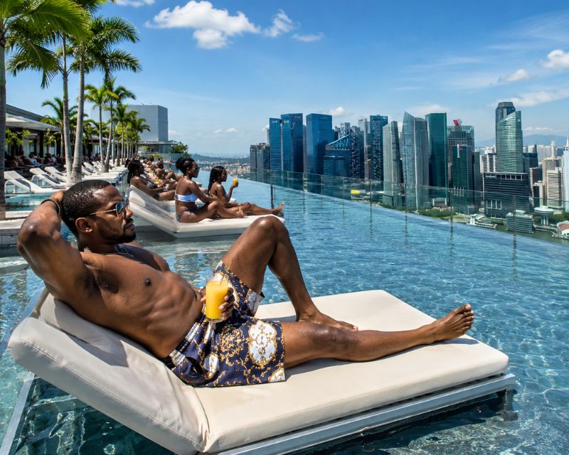 A group of tourists louging on pool chairs in a rooftop infinity pool in singapore